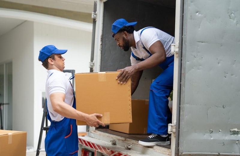 Man movers worker in blue uniform unloading cardboard boxes from truck.Professional delivery and moving service.